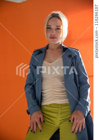 Beautiful fashionable young woman in blue raincoat on orange background Beautiful fashionable young woman in blue raincoat on orange background 118266107