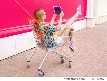 Stylish cool young woman taking selfie with tablet pc in trolley in the city on pink background 118266287