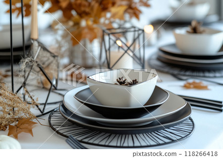 Autumn table setting featuring black dinnerware, candles, and dried fall leaves 118266418