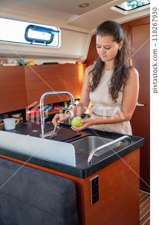 Young woman standing with green apple in kitchen in cabin of modern yacht during sailing in sea. Yacht life concept Young woman standing with green apple in kitchen in cabin of modern yacht during sailing in sea. Yacht life concept 118267930