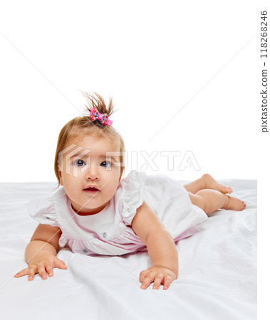 Baby girl lying on her tummy, wide-eyed and curious, with cute pink bow in her hair, exploring her surroundings with soft, innocent gaze. 118268246