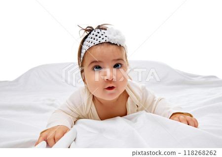 Curious tot in cute outfit peeks over blanket on soft bed with white bedding against studio background. Curious tot in cute outfit peeks over blanket on soft bed with white bedding against studio background. 118268262