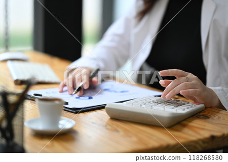 Cropped shot female accountant making calculations and preparing financial data report at desk 118268580