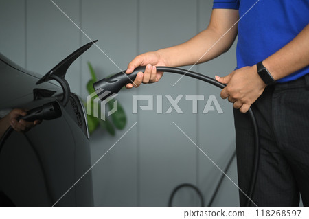 Unrecognizable man plugging in an electric car. Renewable energy and transportation concept Unrecognizable man plugging in an electric car. Renewable energy and transportation concept 118268597
