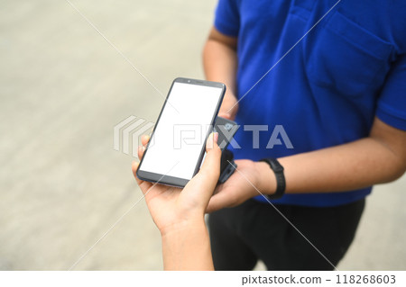 Woman making contactless payment with phone and receiving parcel box from delivery man 118268603