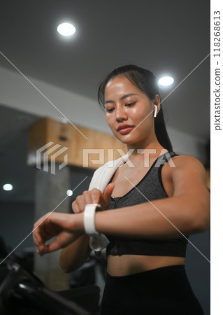 Satisfied female athlete checking her heart rate on smartwatch while exercising in gym. Healthy lifestyle concept 118268613