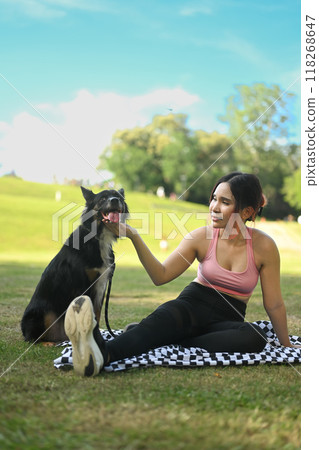 Happy young woman and her border collie dog resting after jogging in a green park 118268647