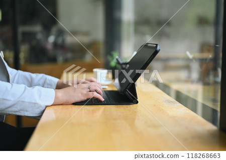 Cropped shot of female freelancer typing on wireless keyboard of digital tablet, working at cafe Cropped shot of female freelancer typing on wireless keyboard of digital tablet, working at cafe 118268663
