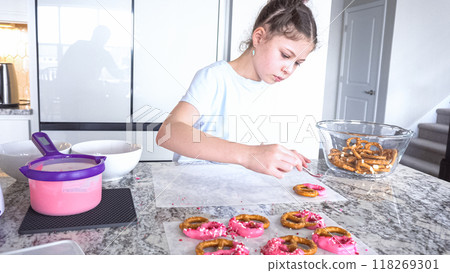 With focused attention, this budding culinary artist dips pretzels into a pot of melted chocolate, creating sweet delights in the warmth of a well-lit home kitchen. 118269301