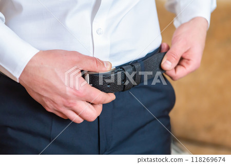 A Man Adjusts His Black Belt While Preparing for a Formal Event in the Evening. A Man Adjusts His Black Belt While Preparing for a Formal Event in the Evening. 118269674