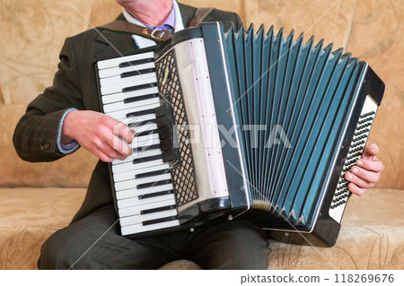 Elderly Man Playing Accordion While Sitting on a Couch in Cozy Living Room. 118269676