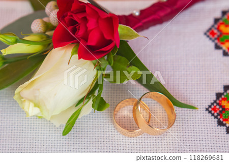 Elegant Wedding Rings Beside a Bouquet With Red and White Roses on a Decorative Cloth. 118269681