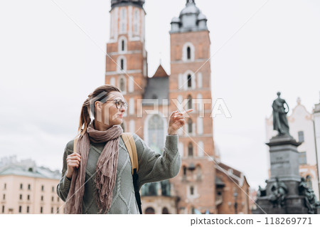 Attractive female tourist is exploring new city. Happy woman with backpack pointing finger on Market Square in Krakow. Traveling Europe in autumn. St. Marys Basilica. Active lifestyle 118269771