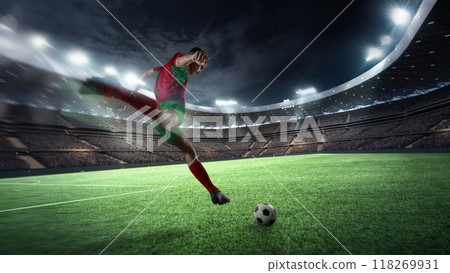 Focused on victory, player kicks ball, it flying across green field, Stadium full of fans charged energy under bright spotlights. Focused on victory, player kicks ball, it flying across green field, Stadium full of fans charged energy under bright spotlights. 118269931