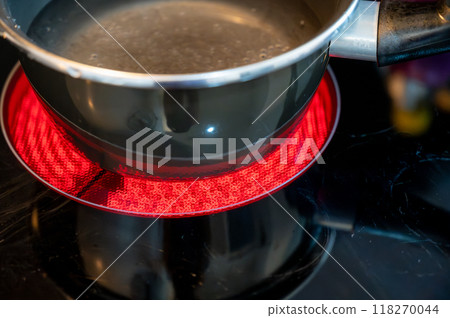 Close-up of a hob with electric hot plates: the heating elements are bright red,the pot of water placed on top is about to boil. Selective focus on the heating elements. Concept of energy consumption 118270044
