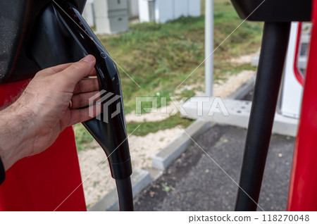 Highway to Budapest, Hungary. August 24, 2022. Charging stations for Tesla electric cars in a highway rest area. Caucasian man's hand grabs the charging socket. 118270048