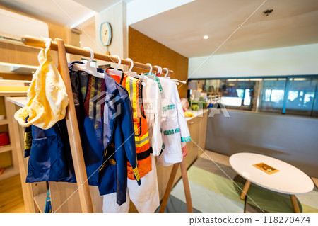 Collection of career uniform for little children on a hanger such as doctor, scientist, engineer and captain in front of any blurry living room background. Collection of career uniform for little children on a hanger such as doctor, scientist, engineer and captain in front of any blurry living room background. 118270474