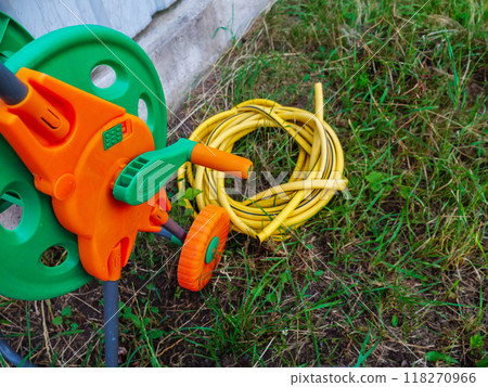 Garden hose reel rests on the grass, next to a neatly coiled yellow hose Garden hose reel rests on the grass, next to a neatly coiled yellow hose 118270966