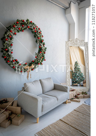 Beautiful interior living room with a big Christmas wreath decorated for Christmas. Big mirror frame with a tree made of balls and toys 118271057