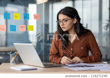 Serious thinking and concentrated focused business woman behind paper work inside office. An employee of the company compares the data of the report with documents, an accountant, auditor at work. 118271290
