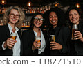 Group of women of different nationalities, dressed in business suits, sitting at bar and relaxing with beer after work. Cozy bar with soft warm light 118271510