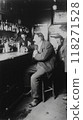 1920s prohibition era. Black and white photograph with man dressed in suit sitting at bar with drink, looking at bartender 118271528