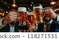 Group of men in business suits raise their glasses of beer, smiling and clinking glasses to celebrate successfully completed project. Warm, cozy bar with soft, light 118271531