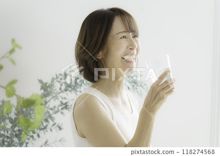 A middle-aged woman drinking a glass of water in the living room 118274568
