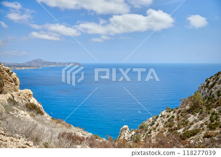 Breathtaking Panoramic View of Calpe's Turquoise Bay from Majestic Cliffside Overlooking Iconic Penon de Ifach Rock Formation. Stunning Costa Blanca Seascape: Calpe's Golden Beaches and Azure Waters 118277039