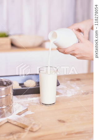 Pouring fresh milk into glass on a wooden kitchen table with baking ingredients 118278054
