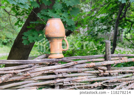Ceramic pot on a wicker fence in countryside. Ethnic art. 118278214