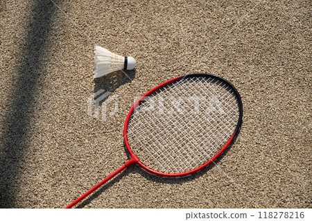 White badminton feather shuttlecock and badminton racket on beige floor sport badminton court in sunny shadow. Summer game outdoors. Close up. 118278216