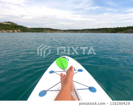 Girl on a SUP board floating on the surface of the blue water of a quarry lake with rocky shores and trees growing on them on a summer day. Summer sports, tourism, recreation, relaxation, travel, rest 118280429