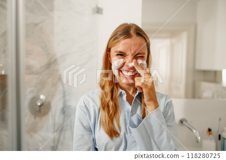 A joyful woman is applying her skincare routine in a stylish and modern bathroom setting 118280725