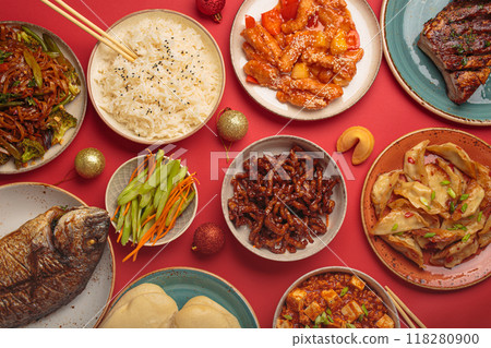 Chinese new year festive table with traditional dishes top view on red background: kung pal chicken, sweet and sour pork, noodles, dumplings, mapo tofu, fish, rice, fortune cookies. Copy space Chinese new year festive table with traditional dishes top view on red background: kung pal chicken, sweet and sour pork, noodles, dumplings, mapo tofu, fish, rice, fortune cookies. Copy space 118280900