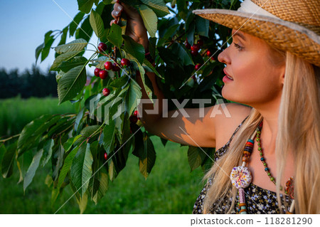 A beautiful woman holds a branch of a cherry tree and watches the summer sun set with delight 118281290