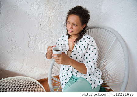 Woman sitting in a modern chair enjoying a cup of coffee in a relaxed setting with a thoughtful expression 118281686