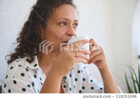 Relaxed woman enjoying a warm beverage at home wearing a polka dot shirt 118281696