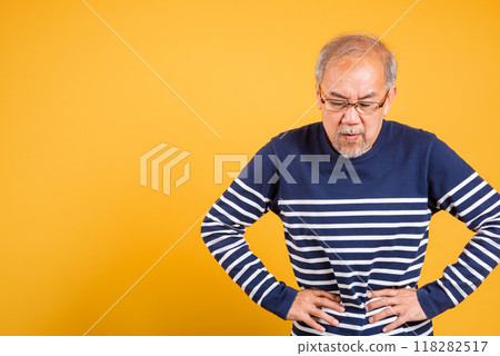 Portrait Asian old man with glasses holds hands on abdomen he stomach ache studio shot isolated yellow background, senior man pensioner feeling pain abdominal pain, hepatitis painful Portrait Asian old man with glasses holds hands on abdomen he stomach ache studio shot isolated yellow background, senior man pensioner feeling pain abdominal pain, hepatitis painful 118282517