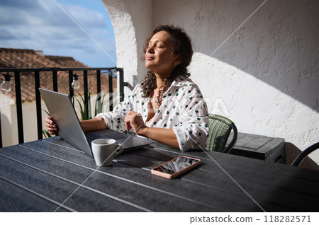 Woman enjoys sunlight on balcony while working on laptop, feeling relaxed and peaceful during a remote work day Woman enjoys sunlight on balcony while working on laptop, feeling relaxed and peaceful during a remote work day 118282571