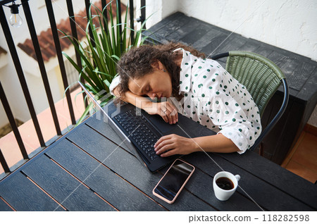 Woman falling asleep on laptop in outdoor workspace during work from home with coffee break 118282598