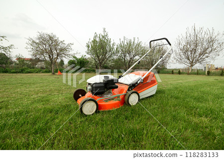 Top view of modern orange-grey gasoline lawn mower cutting bright lush green grass. Gardening work tools. Rotary lawn mower machine on lawn. Professional lawn care service. Place for text Top view of modern orange-grey gasoline lawn mower cutting bright lush green grass. Gardening work tools. Rotary lawn mower machine on lawn. Professional lawn care service. Place for text 118283133