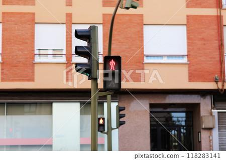 Red traffic light for pedestrian and green light for drivers on city street in front of building facade. Stop signal shows standing man figure on traffic light at pedestrian crosswalk. Regulations 118283141