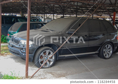An abandoned black car has been standing in one place for a long time. The tires are flat, all in dust, a depressing sight. 118284458