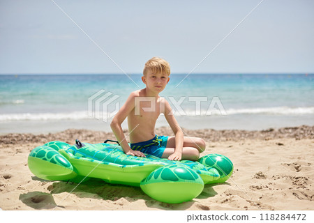 Childhood Beach Bliss: Nine-Year-Old Enjoying Tropical Vacation on Colorful Sea Turtle Float Against Picturesque Coastal Scenery 118284472
