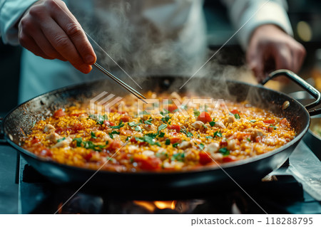 A chef skillfully checks the readiness of vibrant paella on a busy kitchen stove during a lively dinner service in Spain 118288795