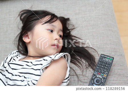3 歲女孩躺在沙發上放鬆看電視 118289156