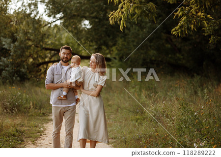 A family of three, a man and a woman with a child in their arms, stand in a park in the summer. A family of three, a man and a woman with a child in their arms, stand in a park in the summer. 118289222