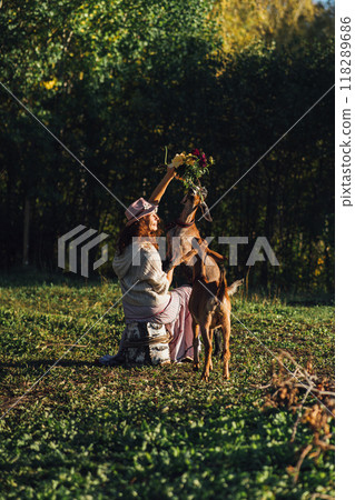 Woman feeding goats with flowers on a farm in a rural landscape Autumn countryside scene with a woman and goats on sustainable farm. Smiling woman in nature caring for goats on an organic farm 118289686