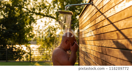 Man enjoying sunset outdoor shower. Concept of relaxation and evening refreshment Man enjoying sunset outdoor shower. Concept of relaxation and evening refreshment 118289772